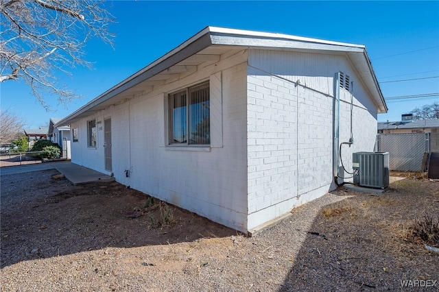 view of side of property with brick siding, fence, and central air condition unit