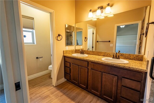 bathroom featuring double vanity, a sink, toilet, and wood finished floors