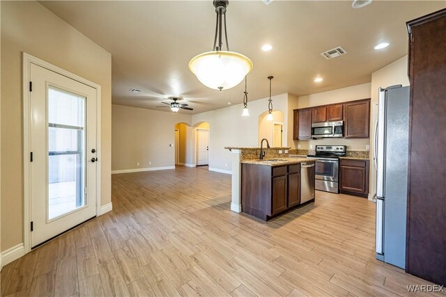 kitchen with light stone counters, arched walkways, pendant lighting, stainless steel appliances, and visible vents