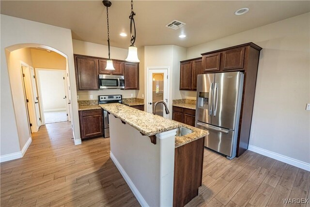 kitchen featuring visible vents, decorative light fixtures, light stone countertops, a kitchen island with sink, and stainless steel appliances