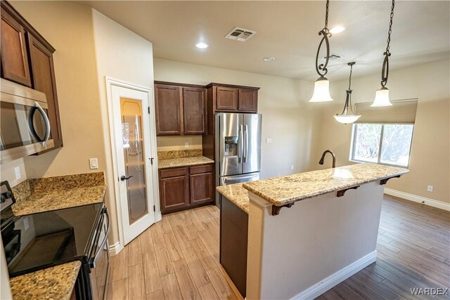 kitchen featuring light stone counters, stainless steel appliances, visible vents, a kitchen breakfast bar, and pendant lighting