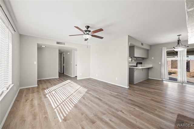 unfurnished living room featuring light wood-style floors, baseboards, visible vents, and a ceiling fan