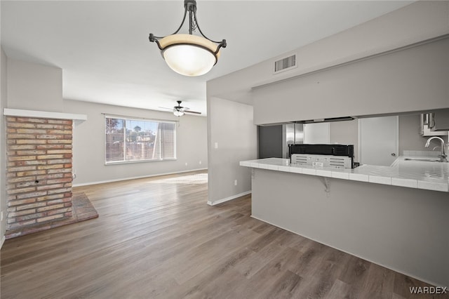 kitchen with tile countertops, white cabinetry, a sink, a peninsula, and a kitchen bar