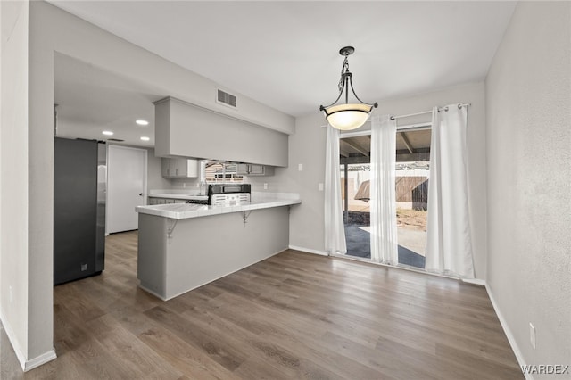 kitchen featuring a peninsula, a breakfast bar, light countertops, gray cabinets, and freestanding refrigerator