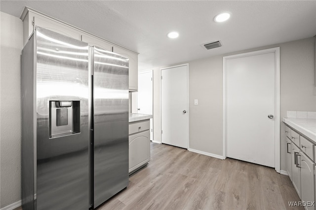 kitchen with light wood-style flooring, recessed lighting, visible vents, light countertops, and stainless steel fridge