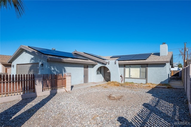 ranch-style house with an attached garage, fence private yard, solar panels, and stucco siding