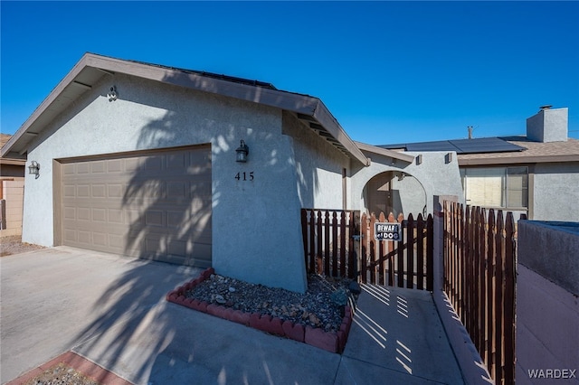 view of side of property featuring stucco siding, an attached garage, roof mounted solar panels, fence, and driveway