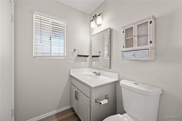 bathroom with toilet, baseboards, wood finished floors, and vanity