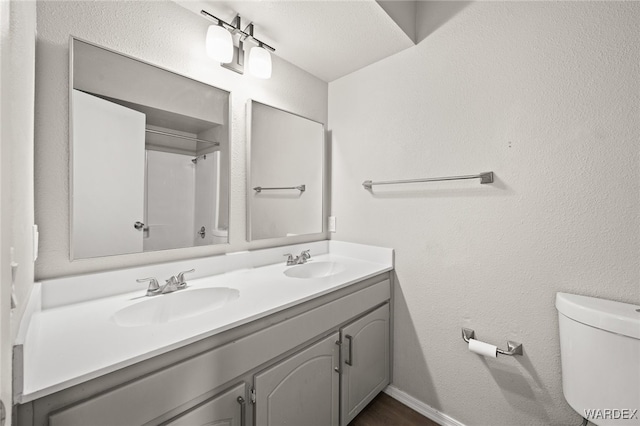 bathroom featuring double vanity, baseboards, toilet, and a sink