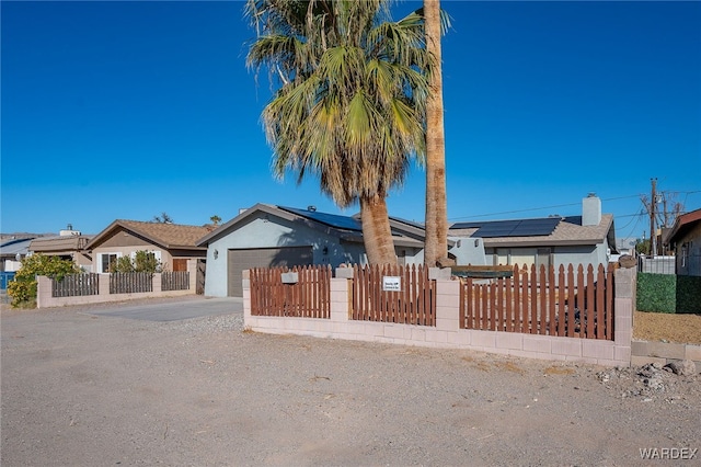 view of front of house featuring solar panels, driveway, a fenced front yard, and an attached garage