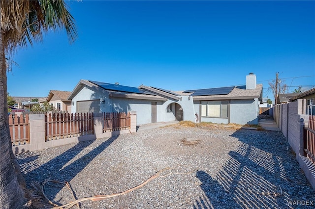 view of front facade with a fenced backyard, a chimney, an attached garage, roof mounted solar panels, and stucco siding