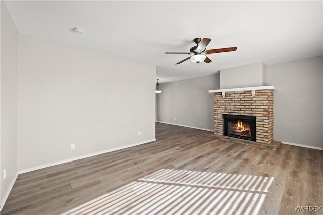 unfurnished living room with ceiling fan, a brick fireplace, wood finished floors, and baseboards