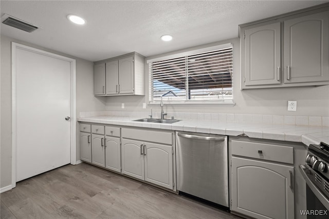 kitchen with tile counters, visible vents, gray cabinetry, a sink, and dishwasher