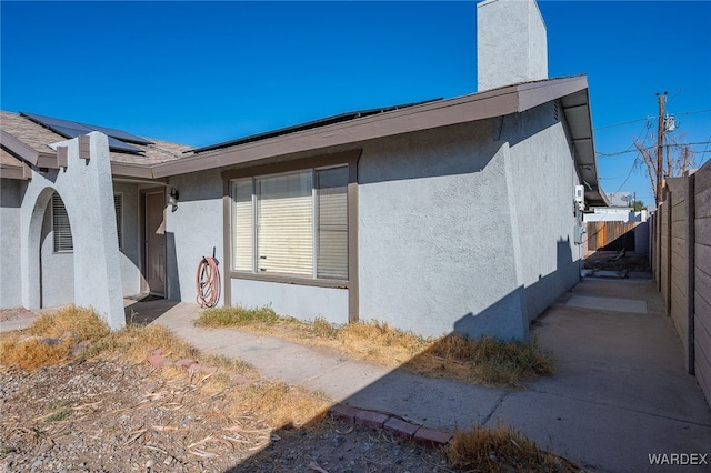 view of property exterior featuring solar panels, a chimney, fence, and stucco siding