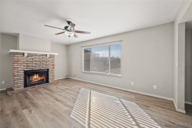 unfurnished living room with light wood-type flooring, a fireplace, baseboards, and ceiling fan