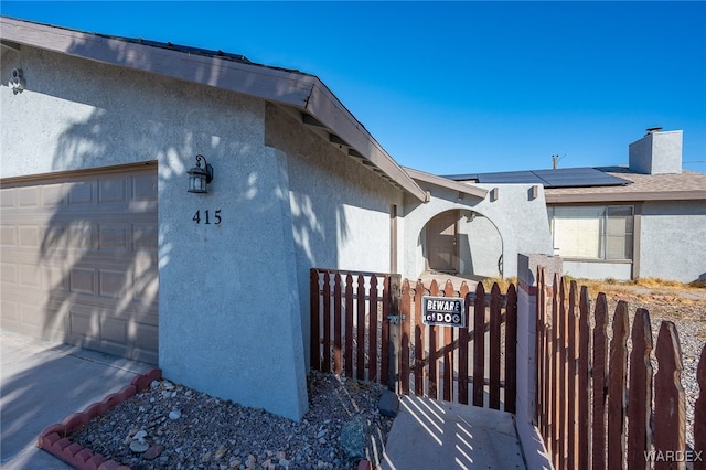 view of side of home with an attached garage, solar panels, fence, a gate, and stucco siding