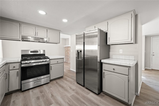 kitchen featuring tile counters, light wood-style floors, gray cabinets, stainless steel appliances, and under cabinet range hood