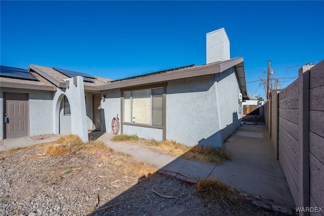 view of home's exterior with roof mounted solar panels, fence, and stucco siding