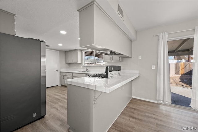 kitchen with a barn door, a peninsula, stove, tile counters, and freestanding refrigerator