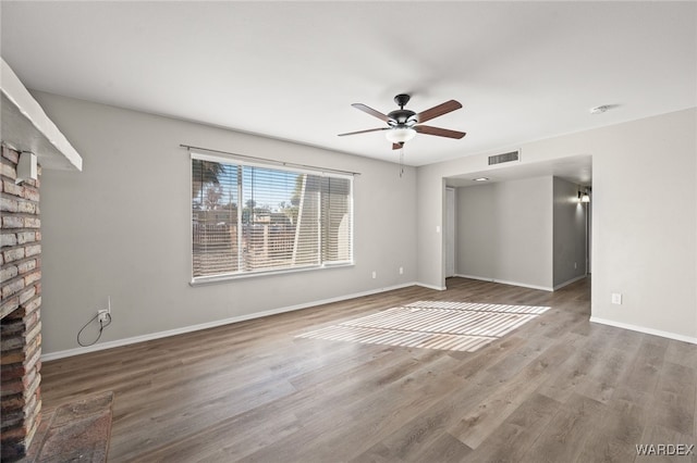 unfurnished living room featuring a ceiling fan, a brick fireplace, visible vents, and wood finished floors