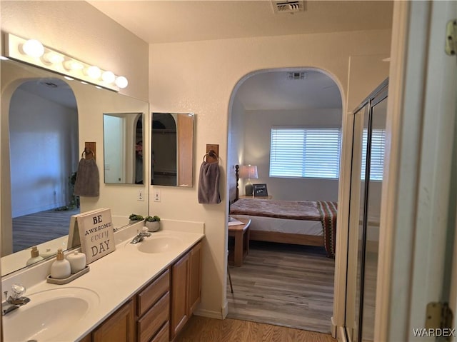 ensuite bathroom featuring a sink, visible vents, wood finished floors, and double vanity