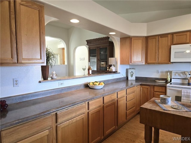 kitchen featuring brown cabinets, light wood-style flooring, dark countertops, recessed lighting, and white appliances