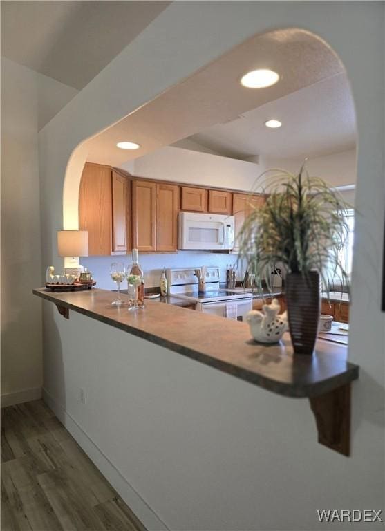 kitchen with brown cabinets, wood finished floors, white appliances, a peninsula, and a raised ceiling