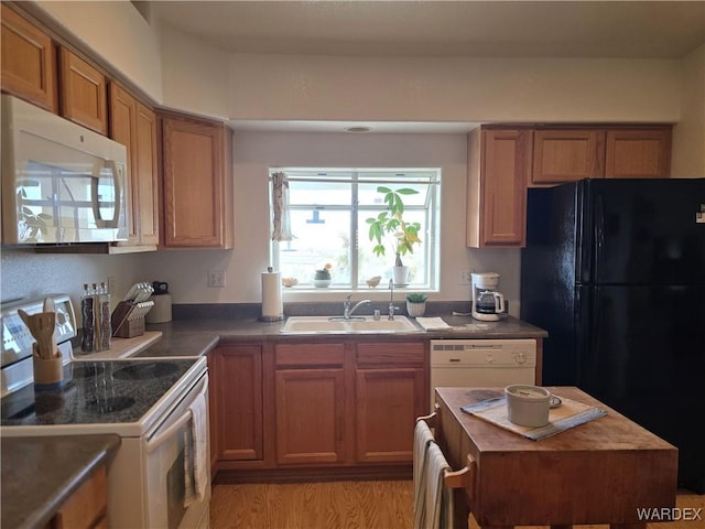 kitchen featuring white appliances, brown cabinetry, a sink, dark countertops, and light wood-type flooring