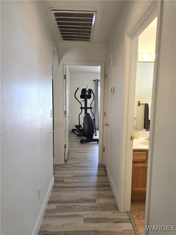 hallway with light wood-style flooring, baseboards, and visible vents