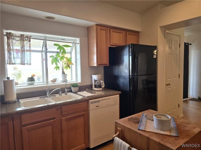 kitchen featuring white dishwasher, freestanding refrigerator, a sink, dark countertops, and brown cabinets