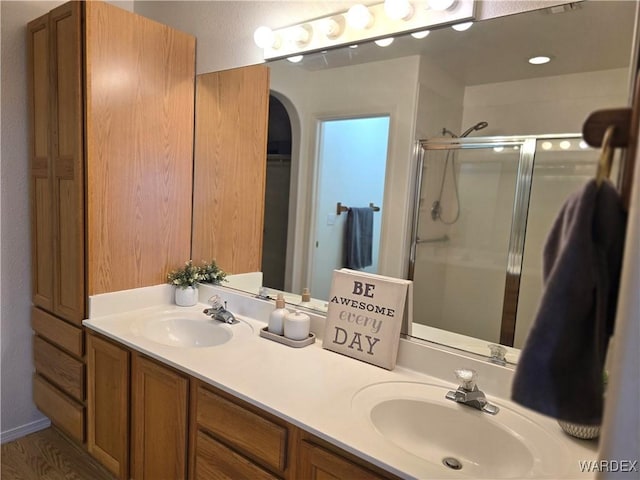 full bathroom with a walk in closet, a shower stall, double vanity, and a sink