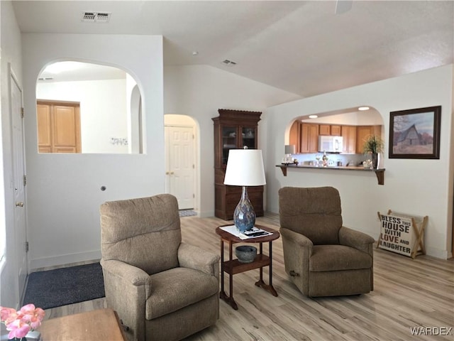 sitting room with lofted ceiling, arched walkways, visible vents, and light wood finished floors