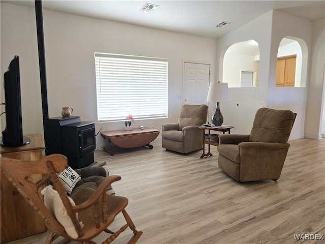 living area featuring arched walkways, visible vents, a wood stove, and light wood-style floors