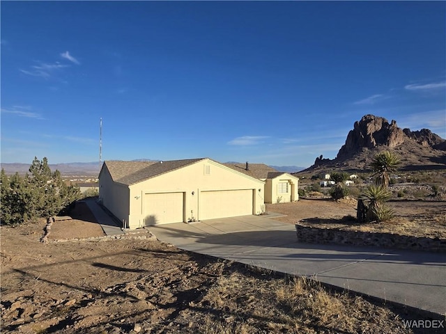 view of side of home with stucco siding, a garage, concrete driveway, and a mountain view