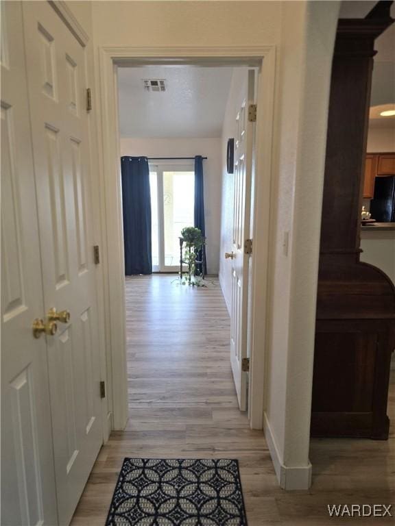 hallway with baseboards, visible vents, and light wood-type flooring