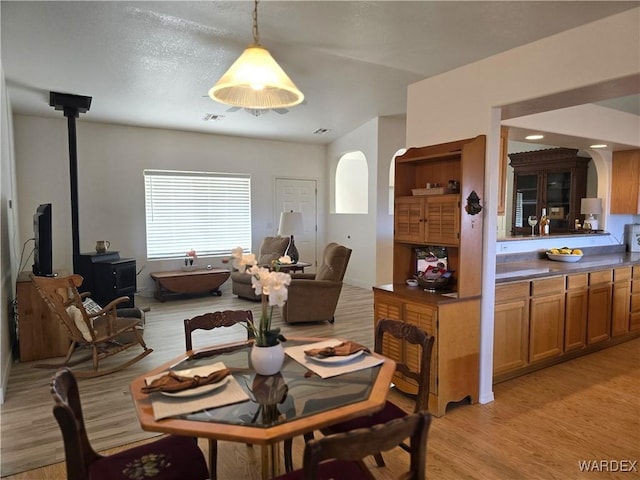 dining space with a wood stove, visible vents, arched walkways, and light wood-type flooring