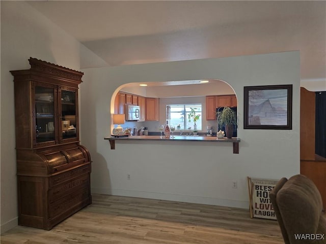 interior space with stainless steel microwave, brown cabinets, light wood-style floors, and baseboards