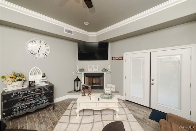 living area featuring visible vents, a fireplace with raised hearth, crown molding, and wood finish floors