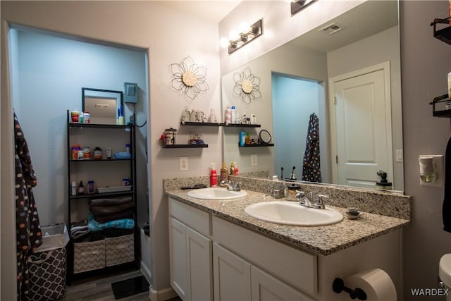 bathroom featuring double vanity, wood finished floors, a sink, and visible vents