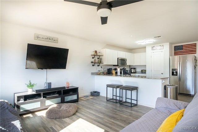 living area featuring a ceiling fan, visible vents, and wood finished floors