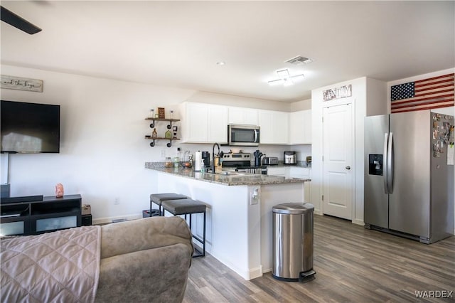 kitchen featuring appliances with stainless steel finishes, dark stone countertops, wood finished floors, a peninsula, and white cabinetry