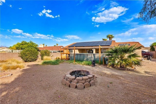 rear view of house with fence private yard, a fire pit, solar panels, and a tiled roof