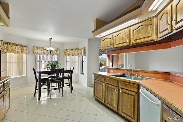 kitchen with light tile patterned floors, a sink, brown cabinets, dishwasher, and pendant lighting