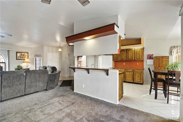 kitchen with brown cabinetry, freestanding refrigerator, open floor plan, a peninsula, and a kitchen bar