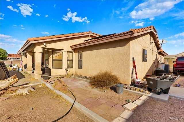 rear view of property featuring a tile roof, fence, central AC unit, and stucco siding