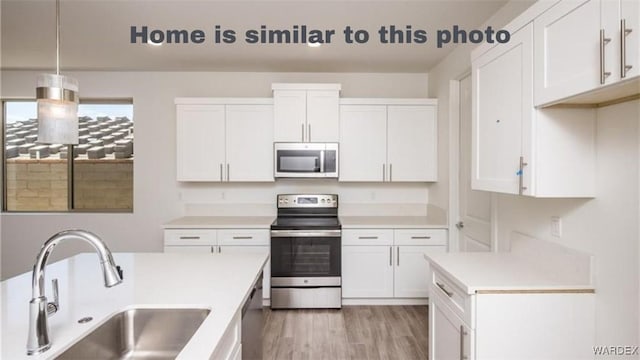 kitchen with a sink, stainless steel appliances, light countertops, light wood-style floors, and white cabinetry