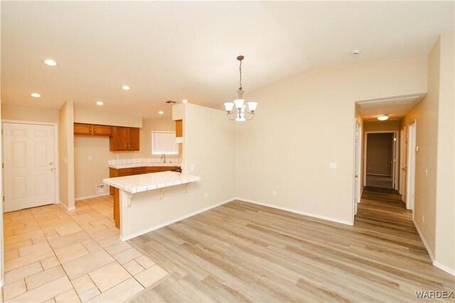 kitchen featuring a peninsula, hanging light fixtures, light wood-type flooring, brown cabinetry, and a kitchen bar