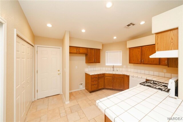 kitchen featuring recessed lighting, a sink, tile counters, and brown cabinets