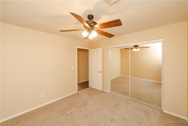 unfurnished bedroom featuring carpet floors, a closet, baseboards, and a ceiling fan