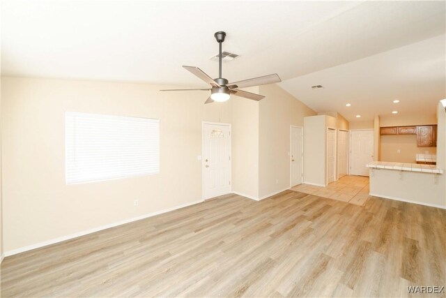 unfurnished living room featuring lofted ceiling, visible vents, light wood-style flooring, ceiling fan, and baseboards